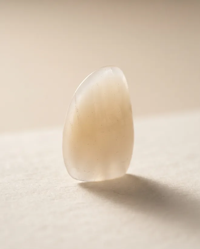 One ultra-thin porcelain veneer shell standing upright on warm off-white paper