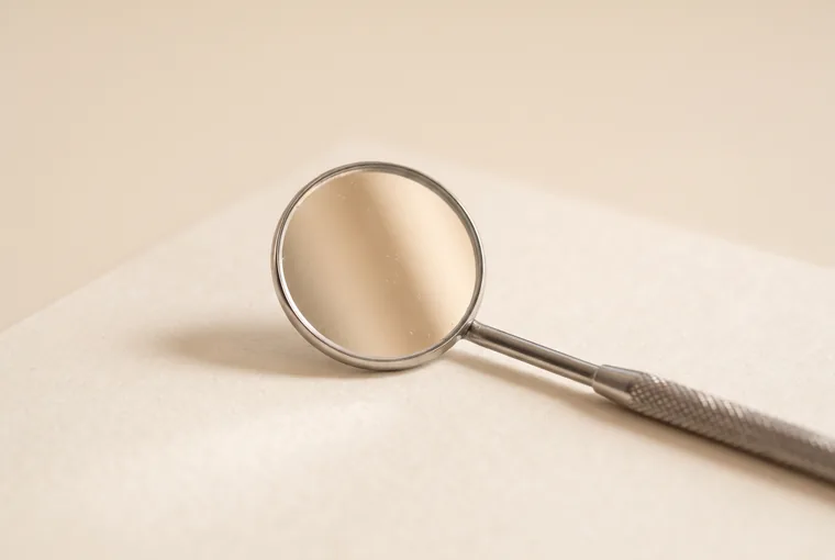 A single round dental mouth mirror lying on warm off-white paper