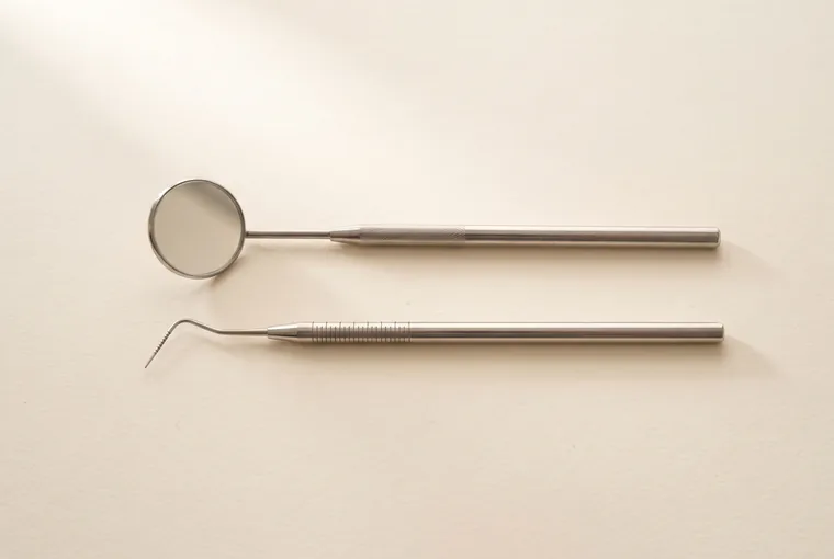 A dental mouth mirror and a periodontal probe resting parallel on warm off-white paper