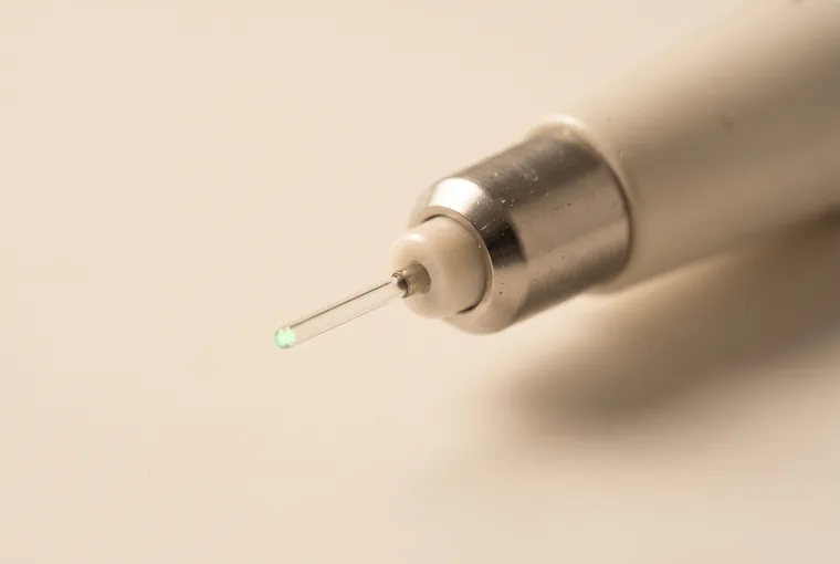 Extreme macro of the fine fibre tip of a dental laser handpiece with a small soft green aiming glow at its very end