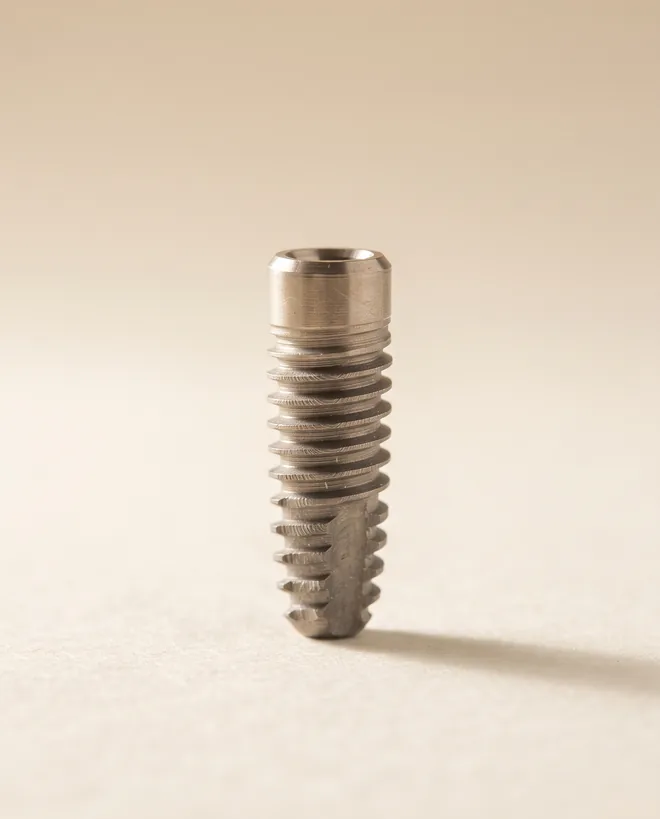 A single titanium dental implant fixture standing upright on warm off-white paper