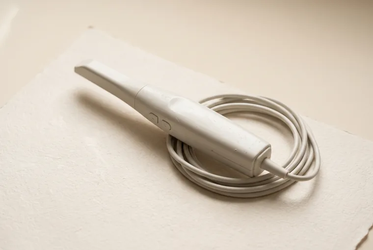 A slim white intraoral scanner wand lying diagonally on warm off-white paper with its cable coiled beside it