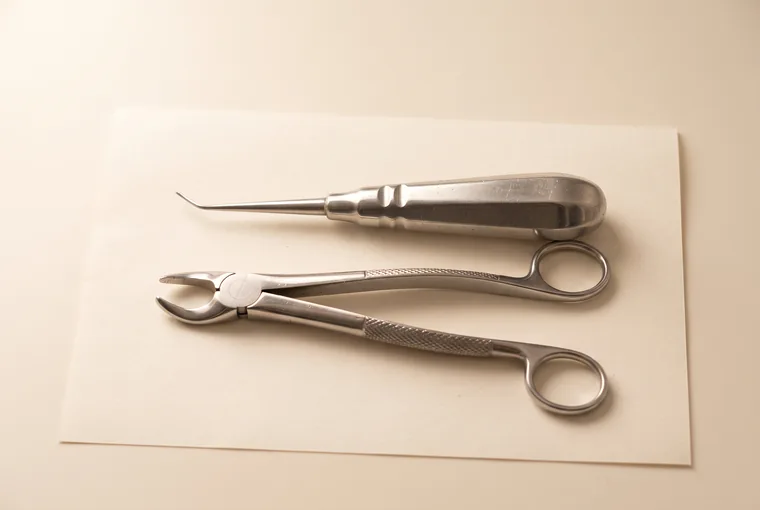 A dental elevator and a pair of extraction forceps laid parallel on warm off-white paper