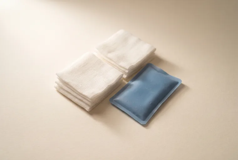 Folded sterile gauze squares and a small soft cold pack arranged on warm off-white paper