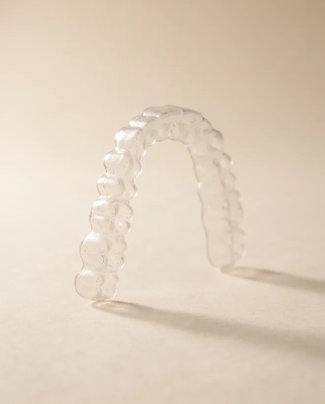 A single clear plastic aligner tray standing upright on warm off-white paper
