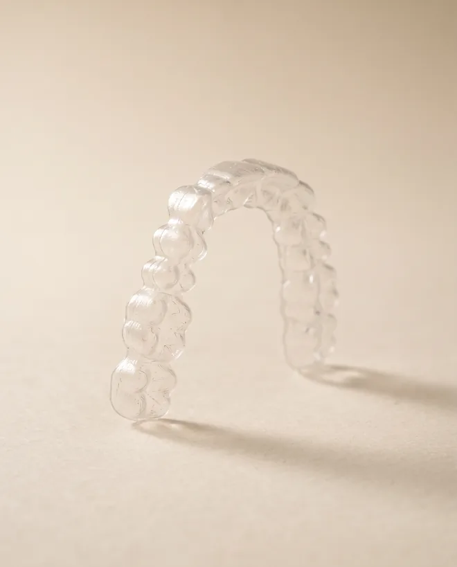 A single clear aligner tray held upright on warm off-white paper
