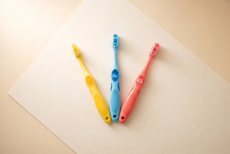 Three brightly coloured children's toothbrushes fanned out on warm off-white paper
