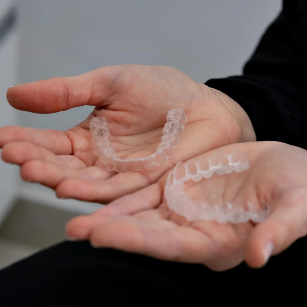 Hands holding removable transparent clear aligners designed for comfortable and nearly invisible teeth alignment